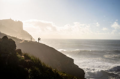 Man photographing on cliff against sea and sky