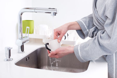 Midsection of woman cleaning utensils in sink