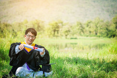 Young man sitting with diploma on field