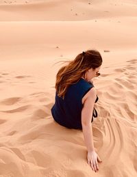 Side view of woman sitting on sand at beach
