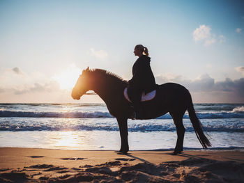 Side view of woman on beach against sky during sunset