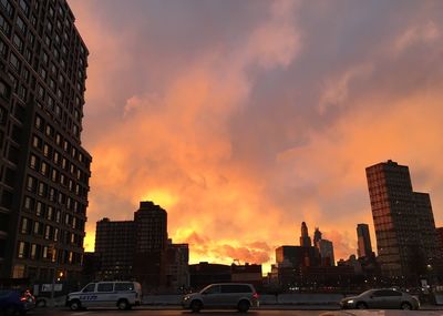 Cars on street by buildings against sky during sunset