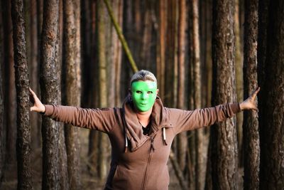 Portrait of woman wearing mask with arms outstretched standing in forest