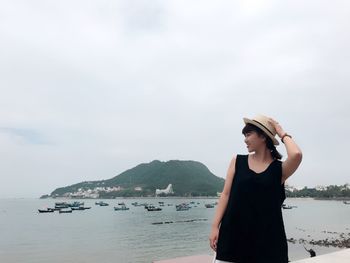 Young woman wearing hat while standing against sea at beach