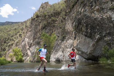 Two men running across a river at the bottom of a canyon in mexico