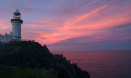 Lighthouse by sea against sky during sunset