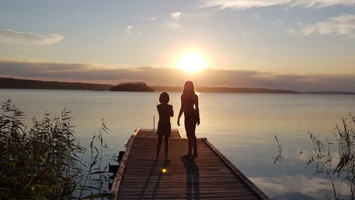 Silhouette people standing on jetty against sea during sunset