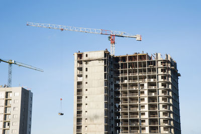 Low angle view of crane by building against clear sky