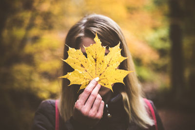 Woman holding maple leaf in front of face during autumn