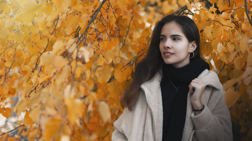 Young woman standing against maple leaves during autumn