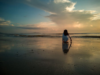 Rear view of woman on beach against sky during sunset