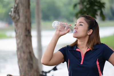 Beautiful young woman drinking water from tree