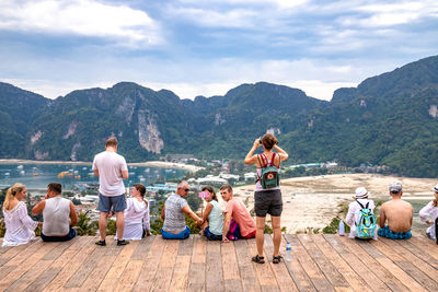 Rear view of people sitting on mountain against sky