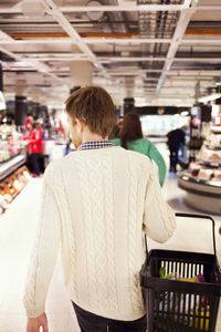 Rear view of man carrying basket while walking at supermarket
