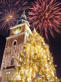 Low angle view of illuminated christmas tree against building at night