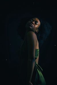 Side view of young woman standing against black background