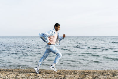 Man wearing clouds denim suit running on footpath against sea