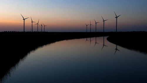 Scenic view of river and wind turbines against sky during sunset