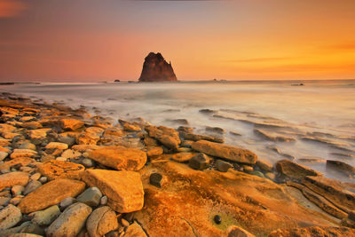 Rocks on sea shore against sky during sunset