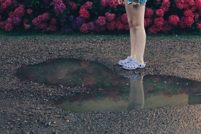 Low section of woman standing by puddle during rainy season