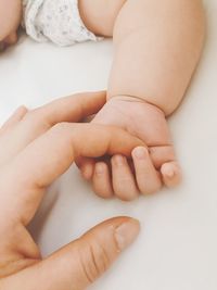 Close-up of toddler baby holding cropped mother hand on bed
