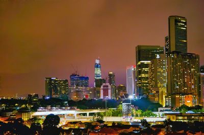 Illuminated modern buildings in city against sky at night