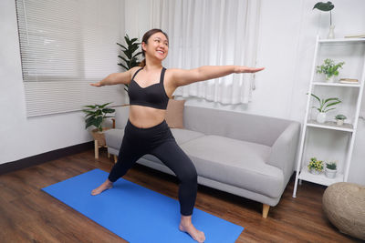 Full length of smiling young woman sitting on floor at home