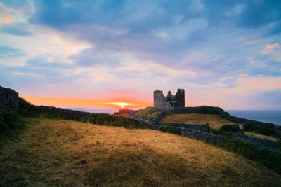 Old castle on field against sky during sunset