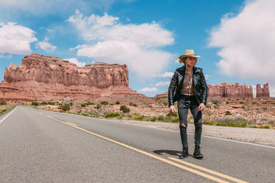 Man standing on rock by road against sky