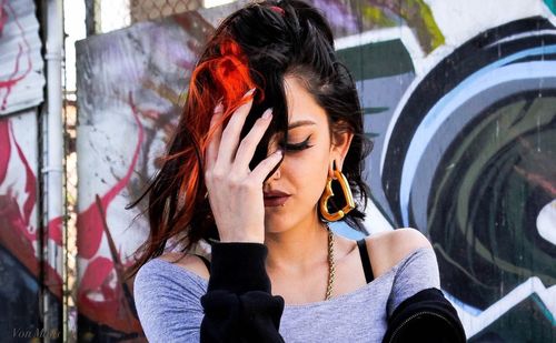 Portrait of woman holding camera while standing against graffiti