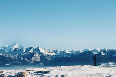 Rear view of man standing on snowcapped mountain against clear sky