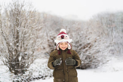 Cute little boy in funny winter hat walks during a snowfall. outdoors winter activities for kids.