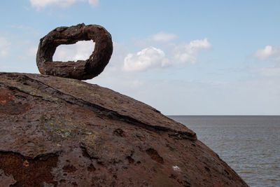 Rusty metal on rock by sea against sky