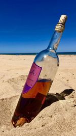 Tilt image of bottle on beach against blue sky