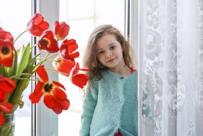 Portrait of smiling girl standing by window at home