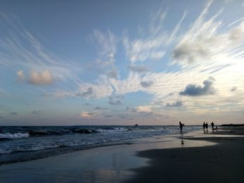 Man walking at beach against sky during sunset