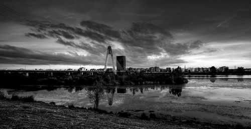 View of buildings by river against cloudy sky