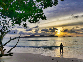 Silhouette woman standing on beach against sky during sunset