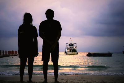 Rear view of silhouette people standing at beach against sky