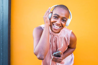 Portrait of smiling woman listening music against yellow background
