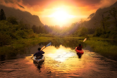 Man in boat on river against sky during sunset