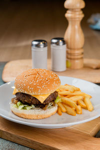 Cheese burger and french fries on white disk with wooden background