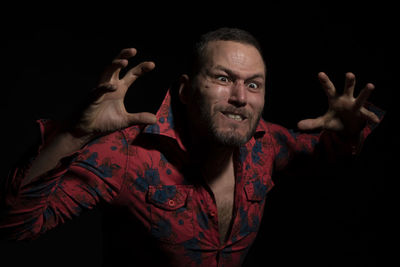 Portrait of smiling man with arms raised against black background