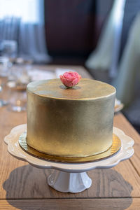 Single tier wedding cake with gold buttercream frosting and edible rose topper.