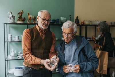 Senior male entrepreneur showing drinking glass to customer in antique shop