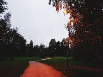 Road amidst trees on field against sky during autumn