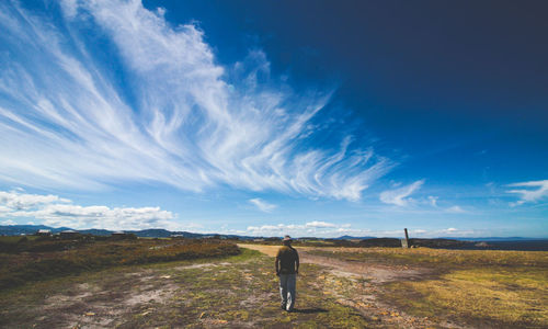 Rear view of man walking on field against blue sky