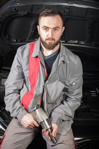 Portrait of male mechanic holding tool while sitting on chair