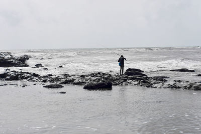Man on rocks by sea against sky