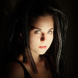 Close-up of portrait of young woman with dreadlocks against black background
